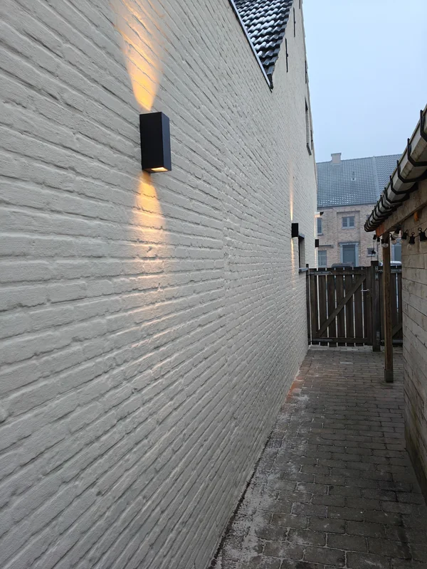 Zwarte wandlampen die een witte bakstenen gevel naar boven en onder verlichten