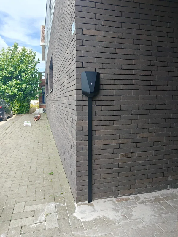 Easee-laadpunt op een donkere gevel met een zwarte kabelgoot tot aan de grond in Houtvenne