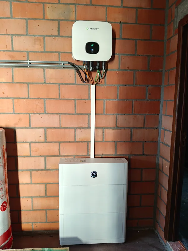 Witte Growatt-omvormer en modulaire thuisbatterij aan een bakstenen muur naast een deur in Itegem