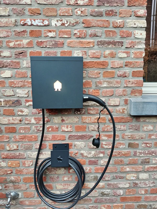 Zwarte Smappee-laadpaal met aangesloten kabel en kabelhouder op een rode bakstenen muur in Westerlo