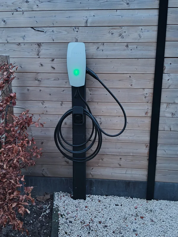 Wit Tesla-laadpunt met kabel op een zwarte montagepaal voor een houten afsluiting in Heist-op-den-Berg